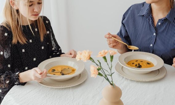 Two women enjoying homemade pumpkin soup at a dining table with floral decor.