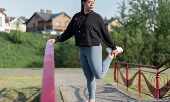 Young woman in activewear stretching on a red railing outdoors.