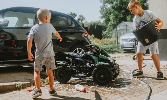 Two kids wash a toy car with soap and water on a sunny day. Fun and playful activity.
